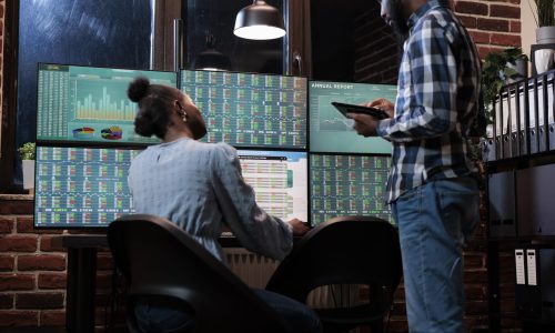 Financial analysts near multi monitor workstation using tablet device to analyze capital profit risks. Hedge fund company professional agents in office, reviewing trading strategies to take profits.